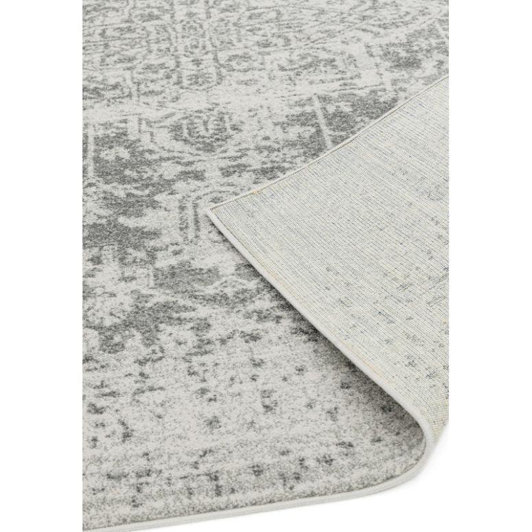 Grey patterned area rug with one corner folded to show backing detail