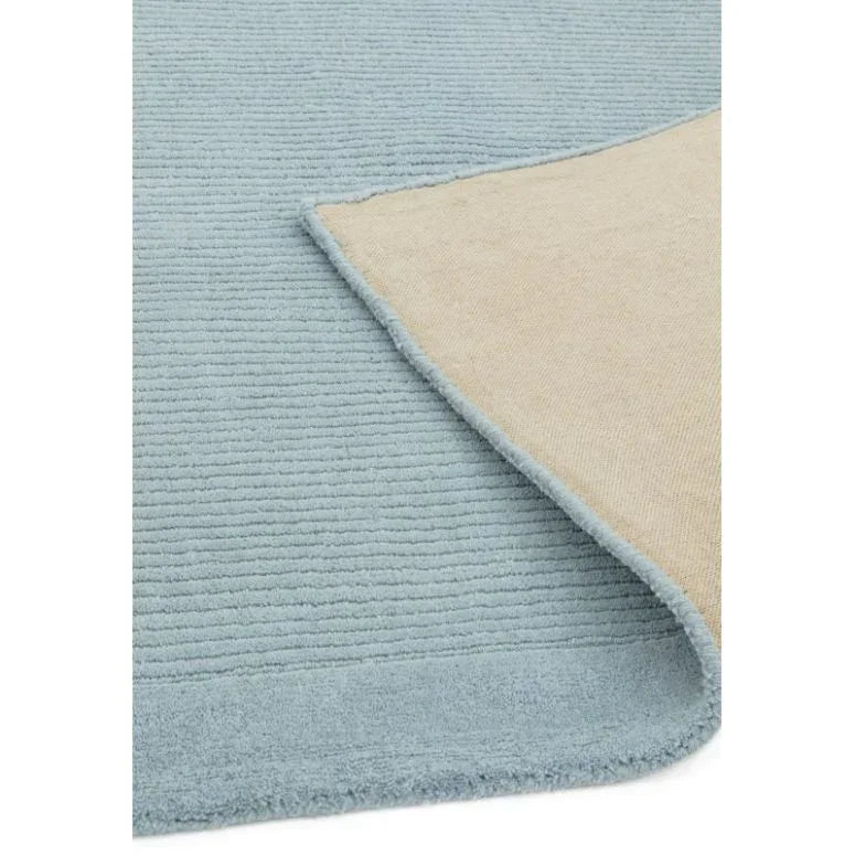 Light blue ribbed area rug with beige underside corner folded
