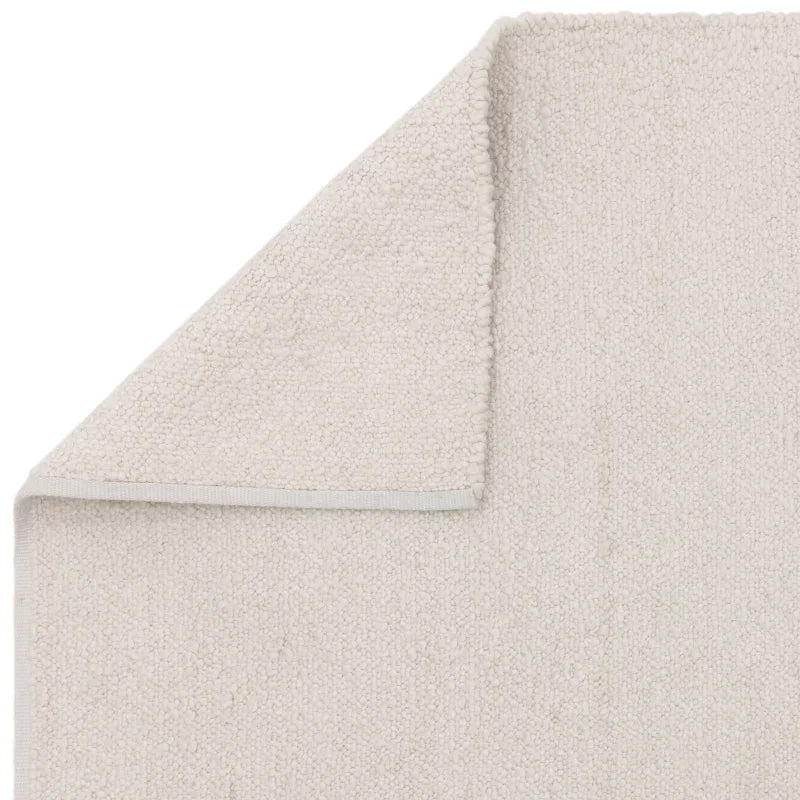 Closeup of cream textured area rug with corner folded to show backing