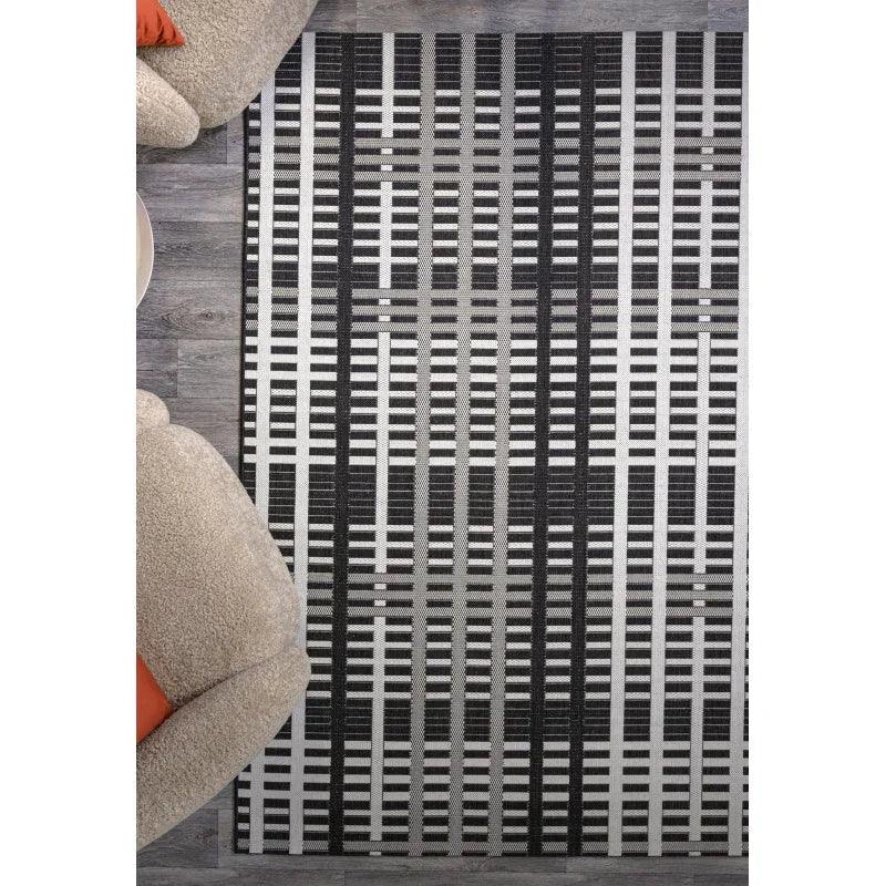Black and grey geometric patterned rug on wooden floor between two armchairs