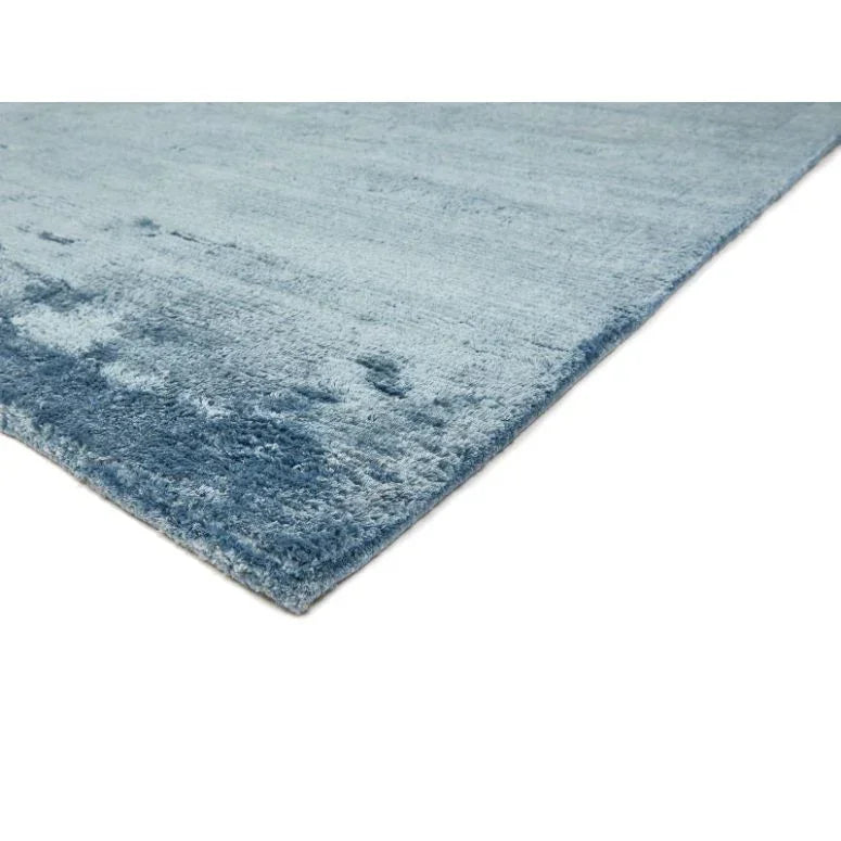 Blue area rug with soft pile and subtle texture, angled corner view on white background