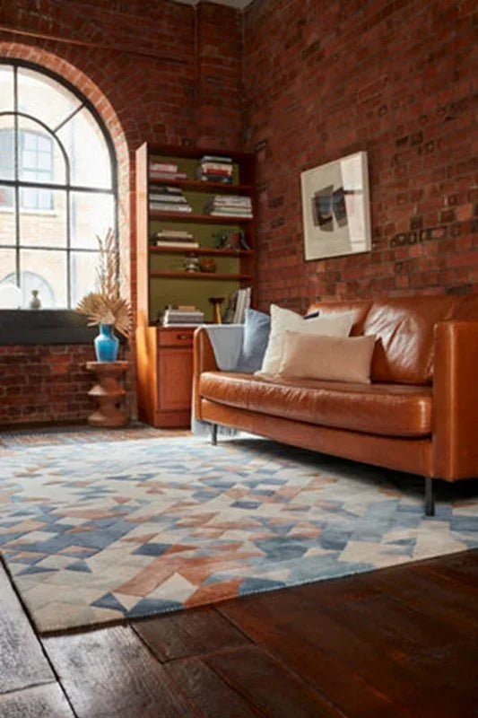 Brown leather sofa with cushions beside bookshelf on patterned area rug in brick living room