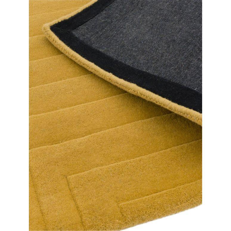Close-up of mustard yellow rug with textured geometric pattern and black fabric backing