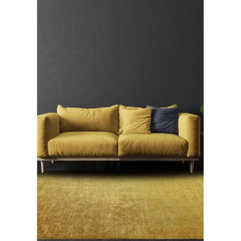 Yellow velvet sofa with plush cushions and navy accent pillow against dark wall