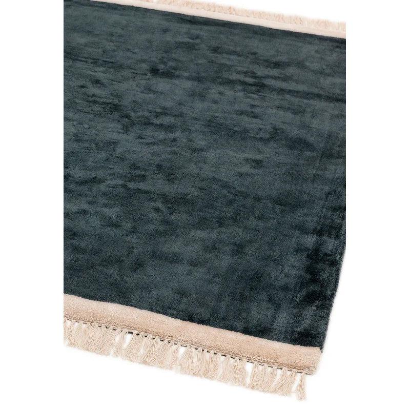 Dark grey area rug with beige fringe border and soft textured surface, corner view