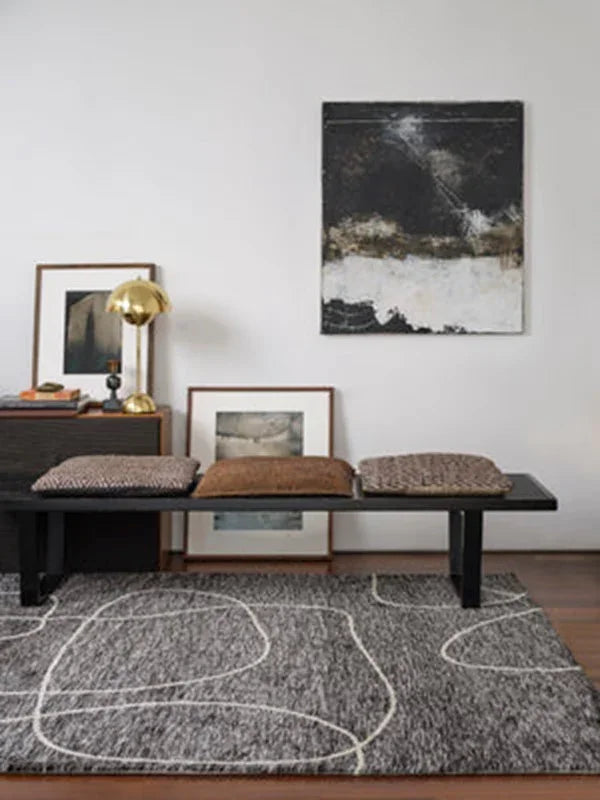 Modern black bench with textured cushions on grey patterned rug in living room setting
