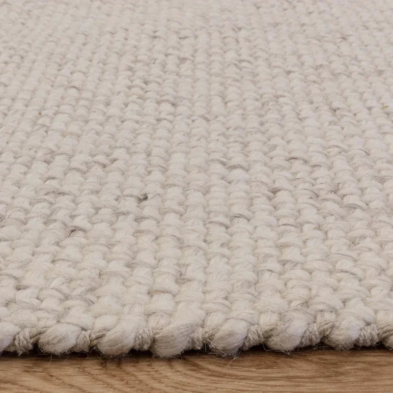 Textured cream wool rug on wooden floor, close view of woven detail and edging