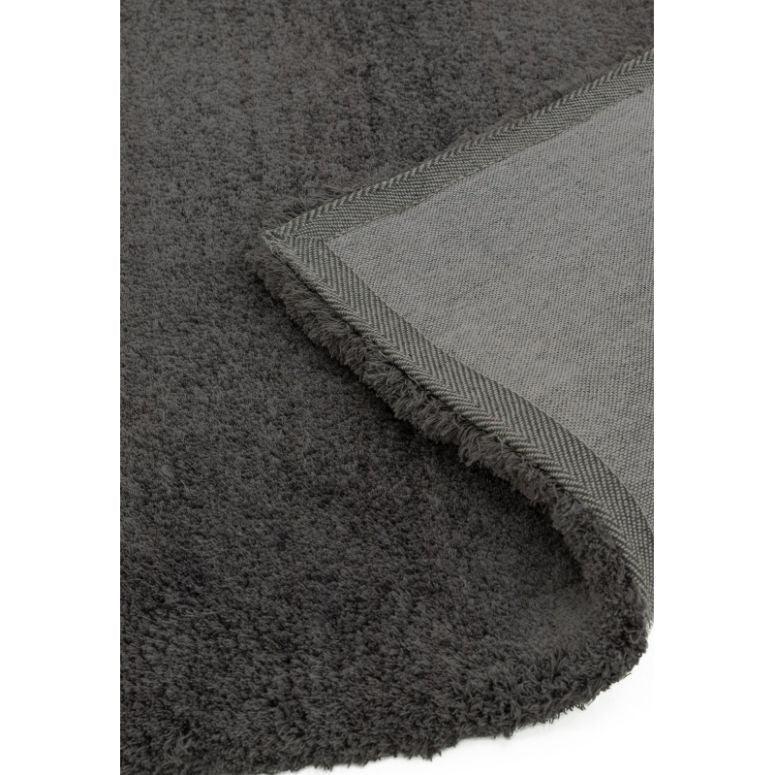 Close up of dark grey rug with soft pile and fabric edging, corner folded to show backing