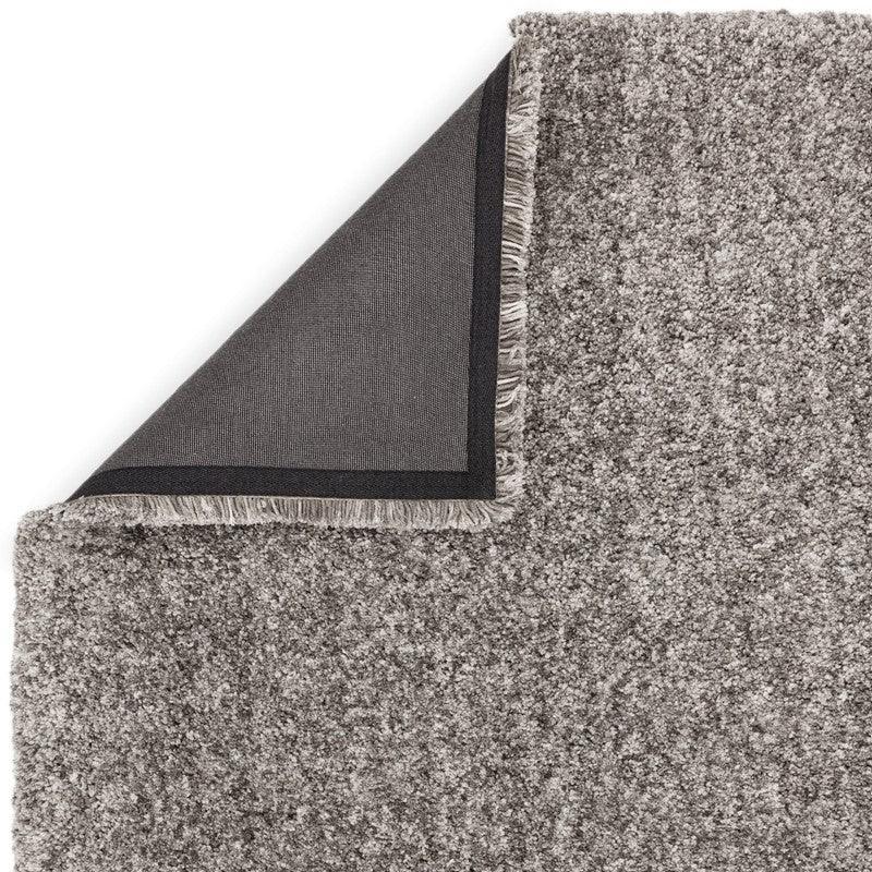 Grey shaggy rug close-up with corner folded to show backing and texture detail