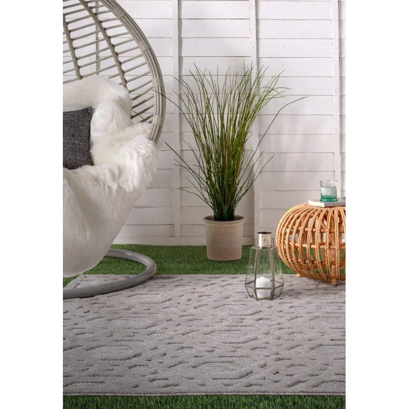 Modern grey outdoor rug on artificial grass beside egg chair and wicker side table