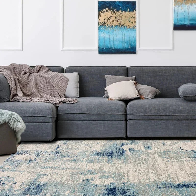 Grey fabric corner sofa with scatter cushions and throw, abstract blue area rug in living room