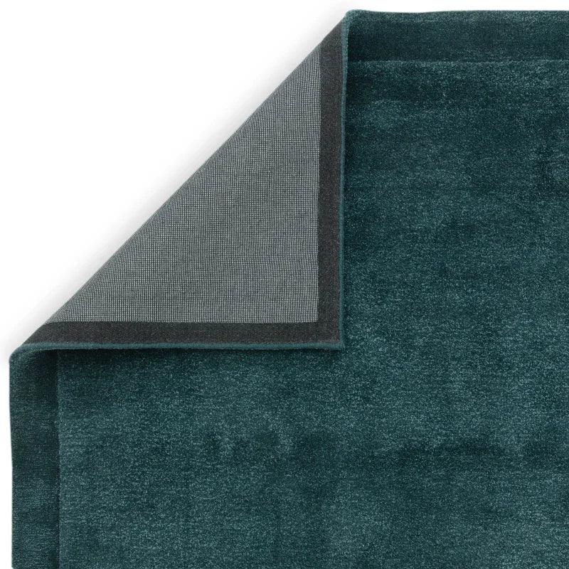 Close-up of dark green area rug with corner folded to show textured backing