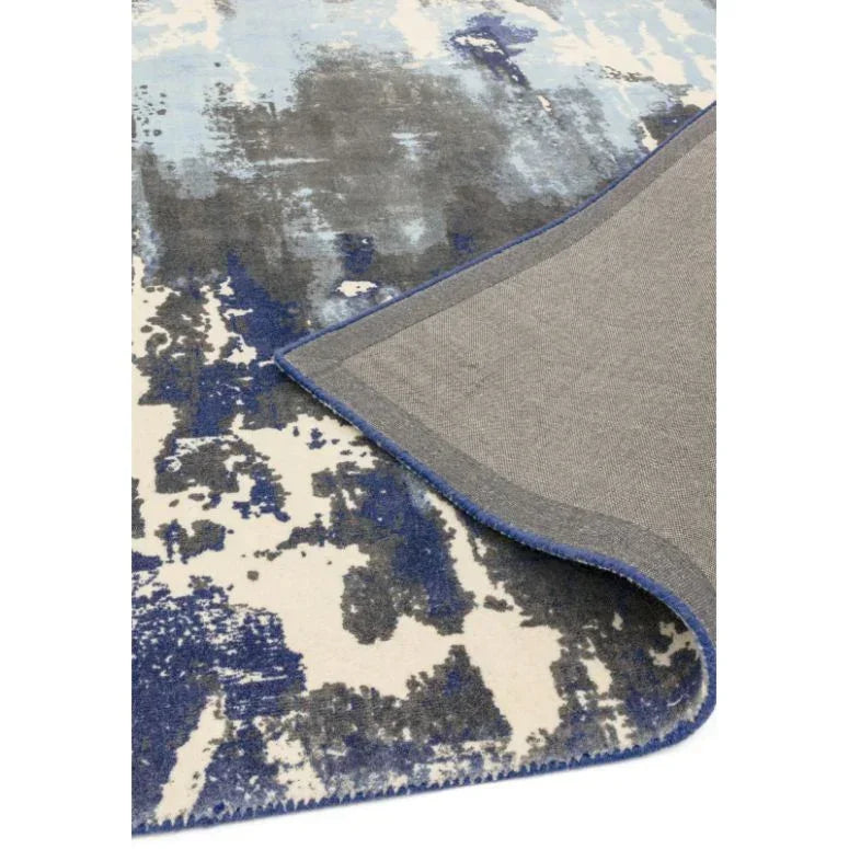 Blue abstract pattern area rug with corner flexed to show backing