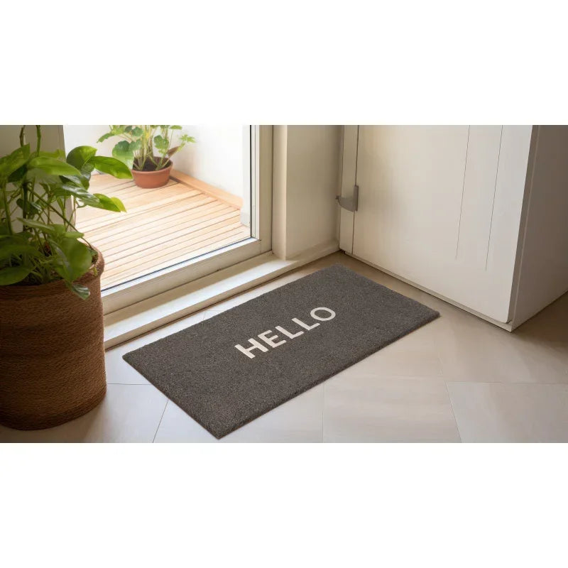 Grey door mat with white hello text placed by indoor entryway near plants
