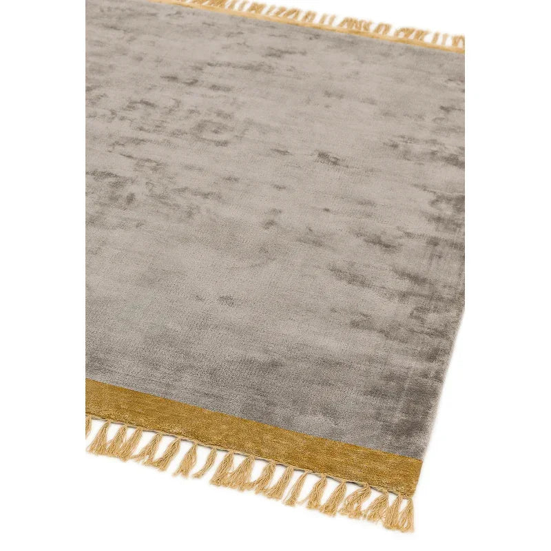 Grey area rug with gold border and tasseled fringe detail, corner angle view