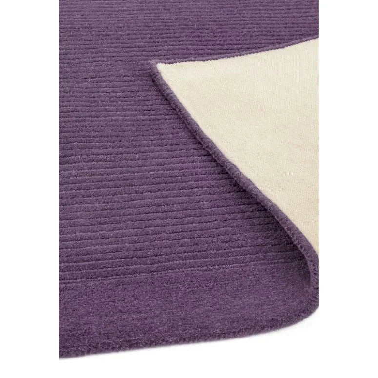 Close up of purple textured area rug with corner lifted showing cream backing