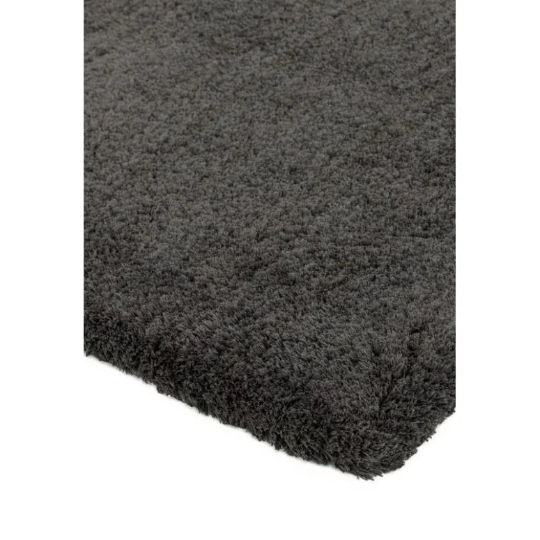 Dark grey shaggy rug with thick pile, close-up of corner on white background
