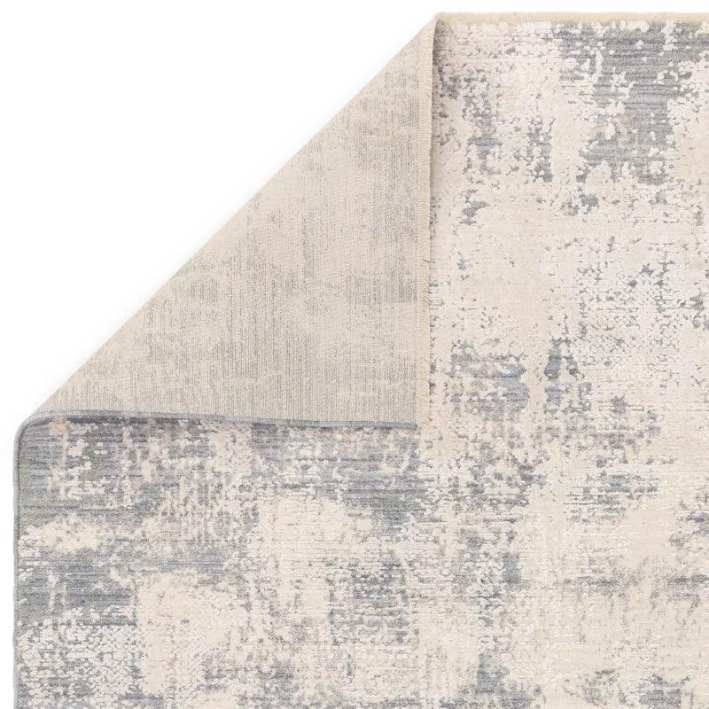 Abstract cream and grey area rug with folded corner showing backing detail