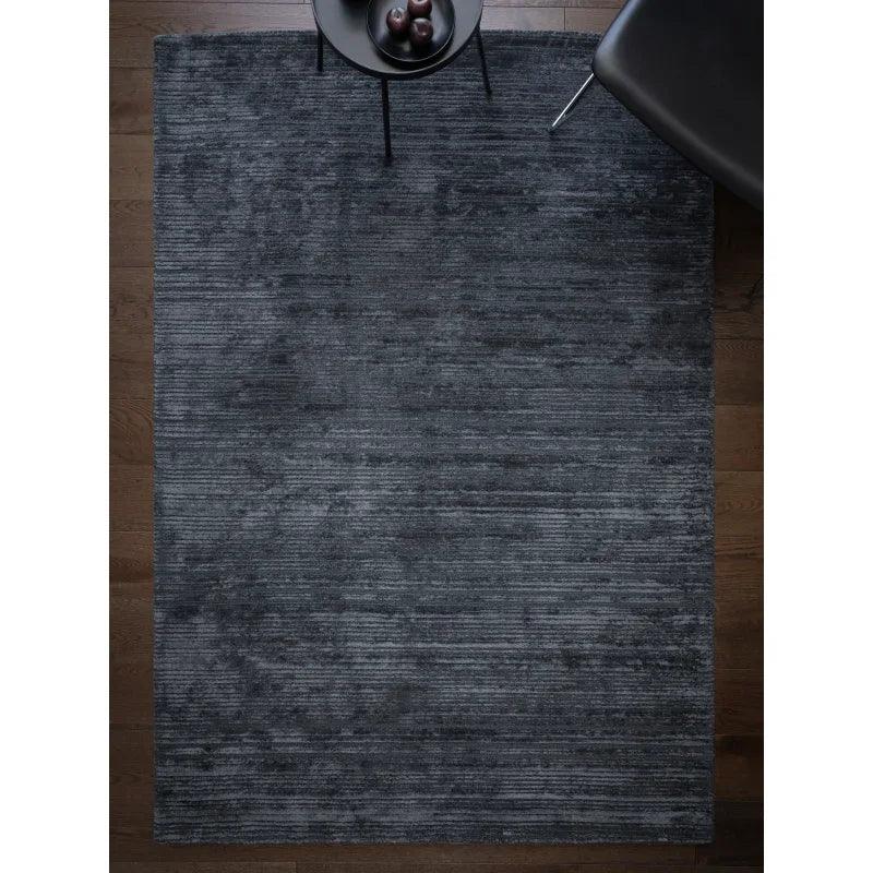 Charcoal textured area rug on dark wood floor beside black chair and side table