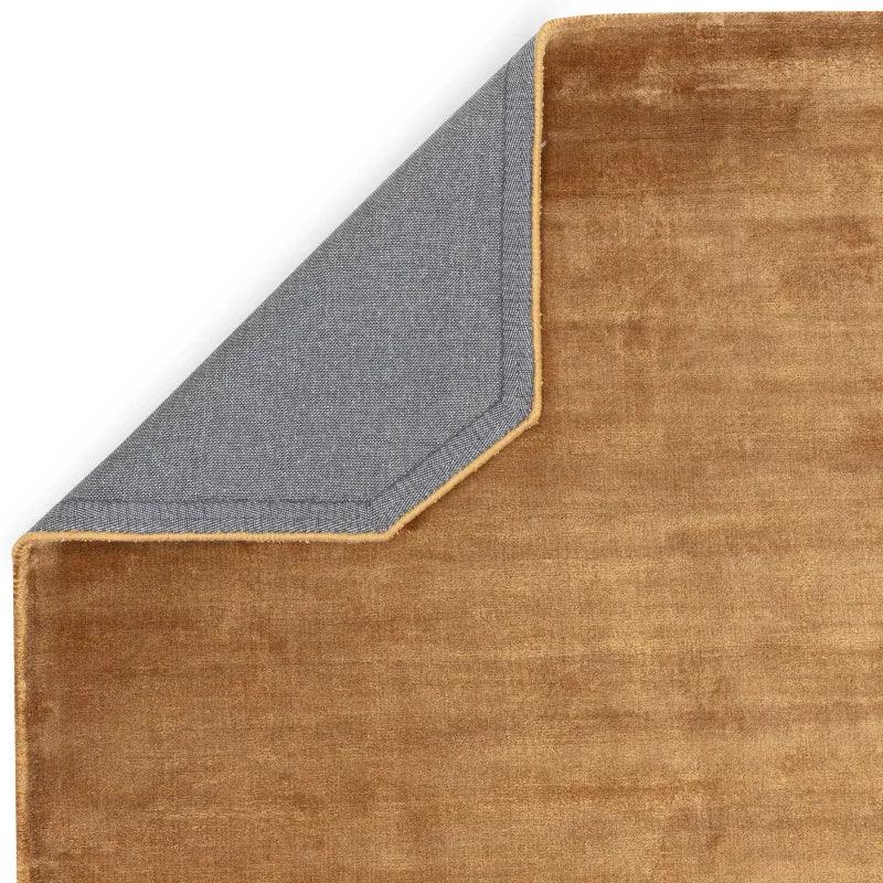 Corner view of tan velvet area rug with corner folded showing grey fabric backing