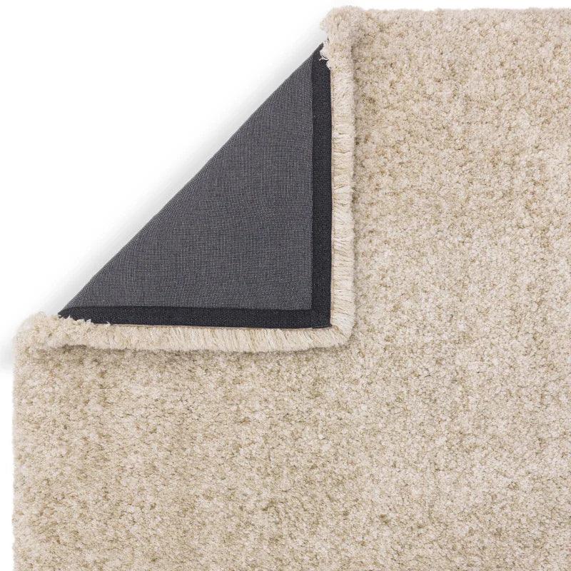 Beige shaggy rug with corner flipped to show black non-slip backing