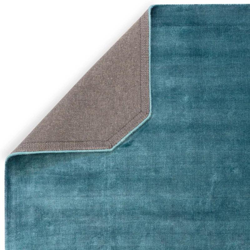 Teal velvet area rug with corner flipped to show grey backing fabric detail