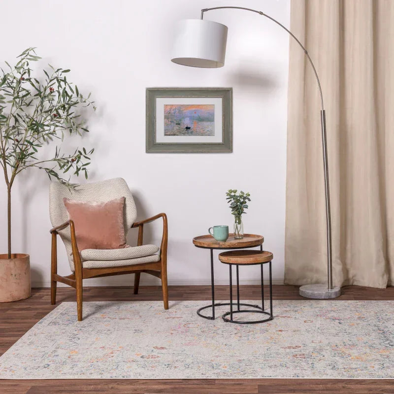 Modern accent chair with cushion, round wooden nesting tables and floor lamp in cosy living room