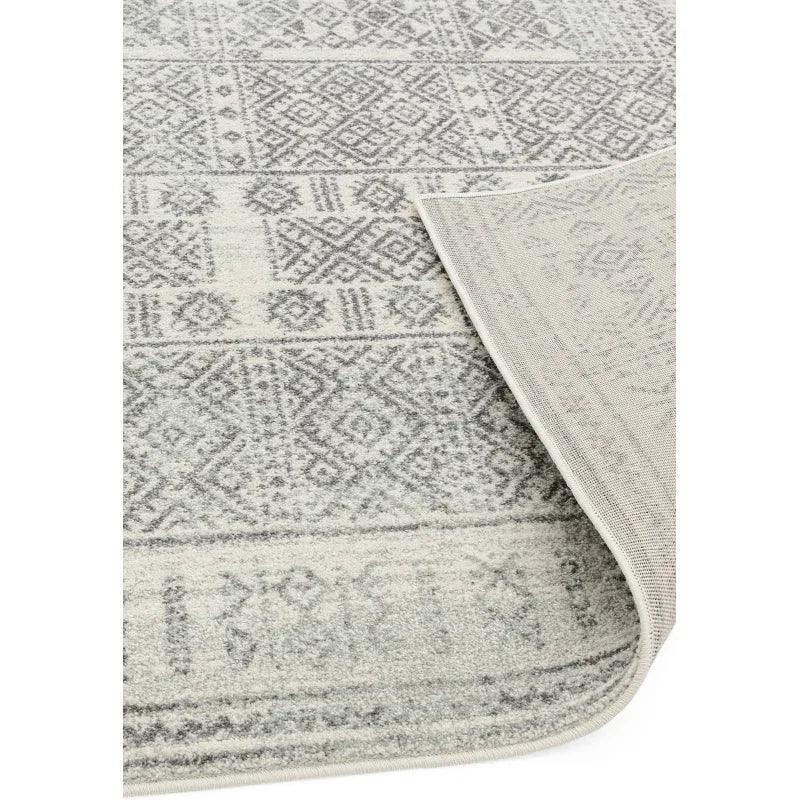 Grey patterned area rug with geometric design and folded corner showing backing