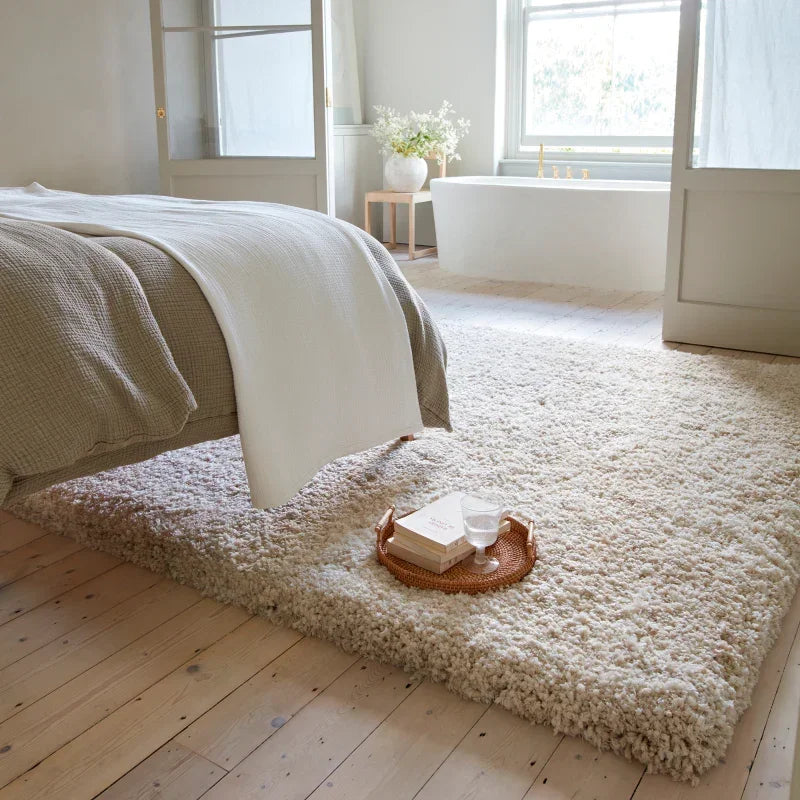 Plush cream shaggy rug in bedroom beside bed with tray holding books and glass