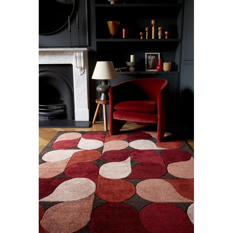 Red and beige geometric rug on wood floor with velvet accent chair in living room setting