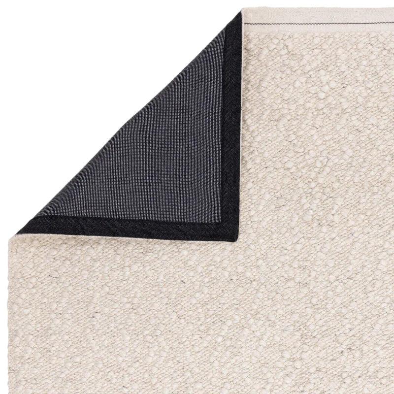 Cream textured rug with corner flipped to reveal black non-slip backing