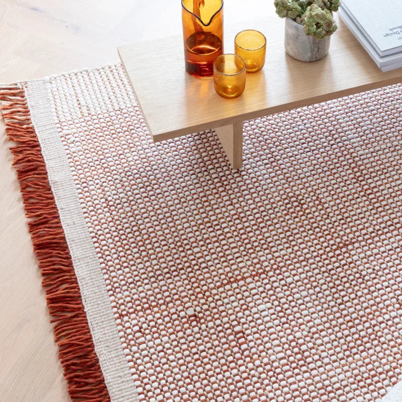 Textured woven rug with red fringe under wooden coffee table with amber glassware