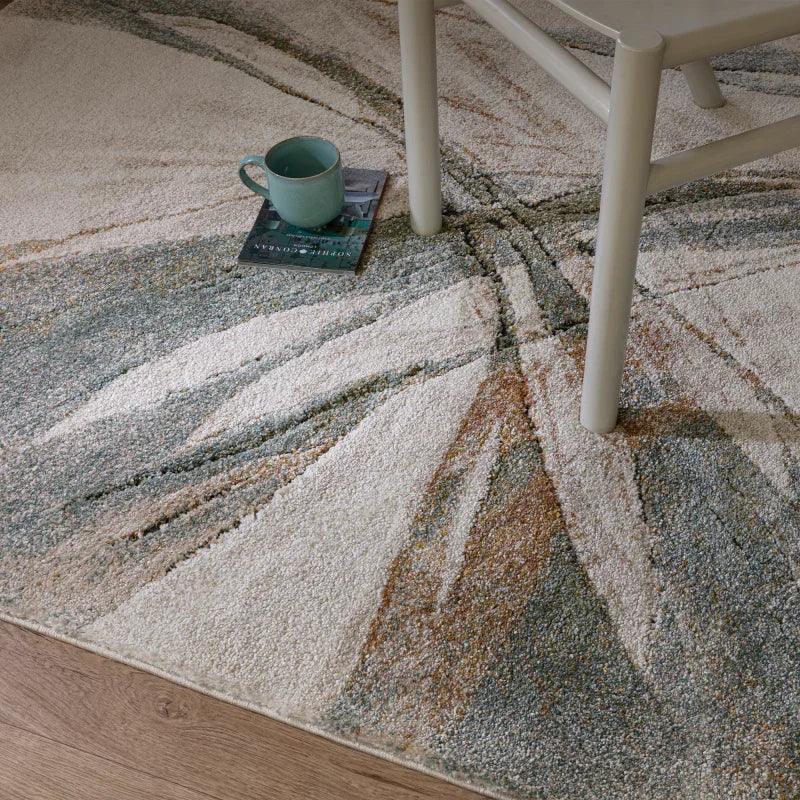 Abstract patterned area rug with neutral tones, chair leg, and mug on a book