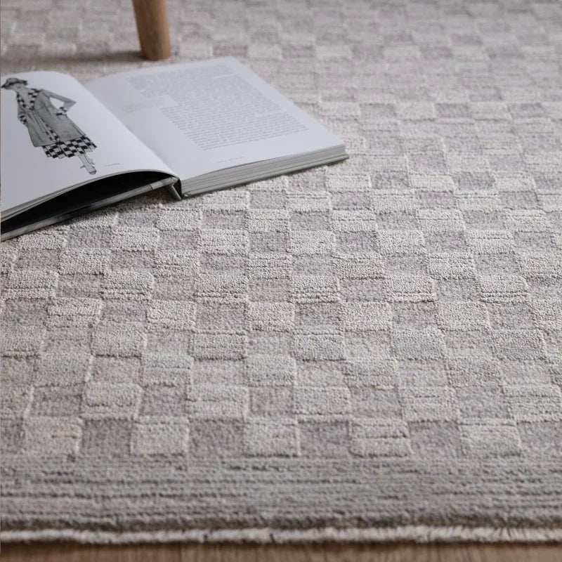 Textured beige rug with geometric pattern placed on wood floor beside an open book