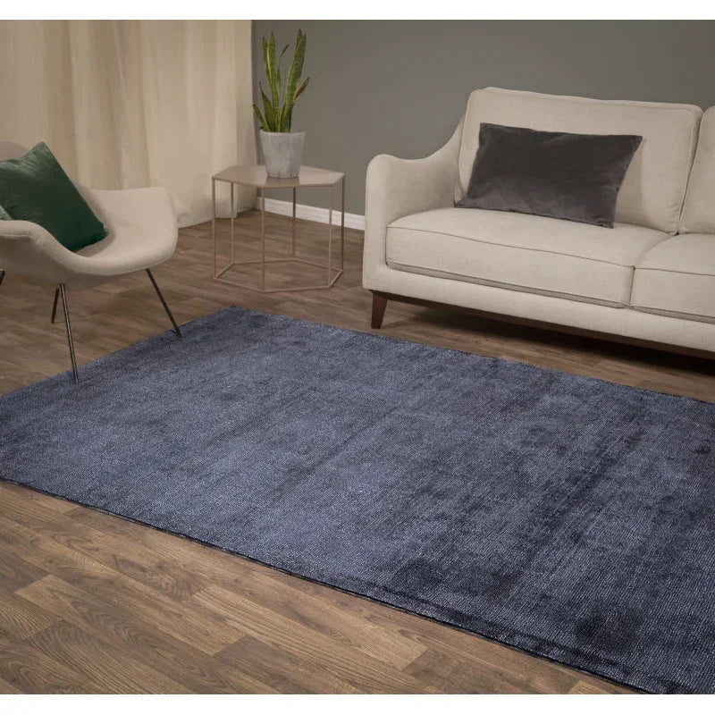 Dark blue area rug on wood flooring between beige sofa and modern chair in living room