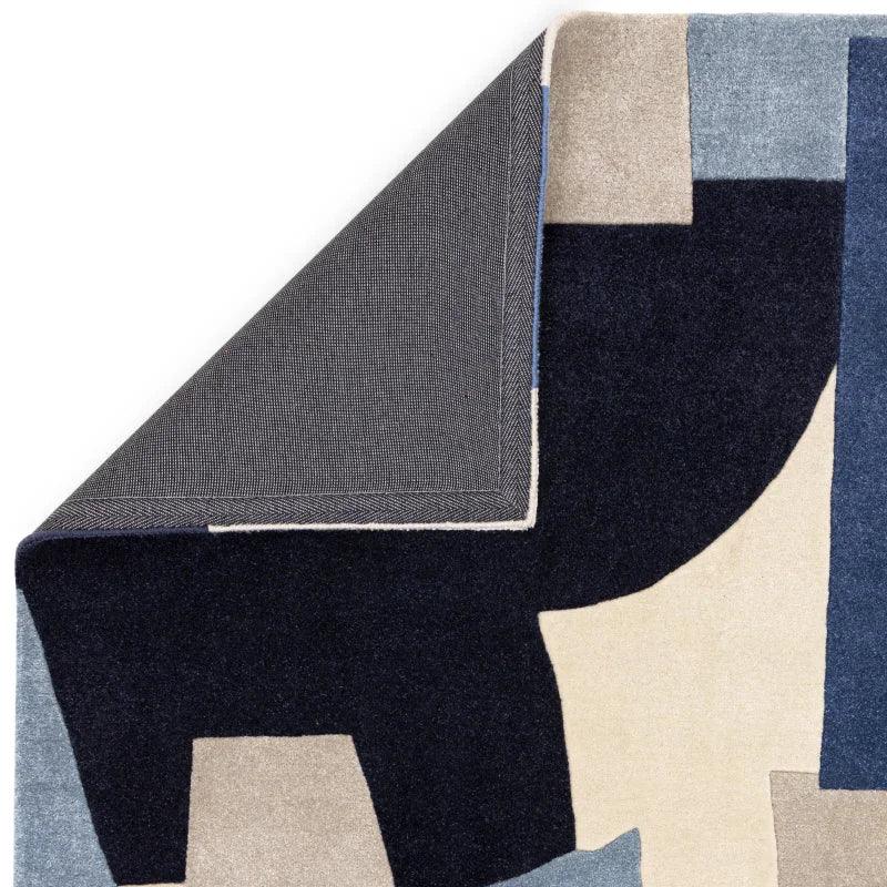 Modern abstract area rug with navy, beige, and blue geometric pattern, corner folded