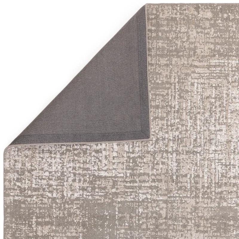 Abstract patterned area rug in beige and grey with visible corner fold showing backing