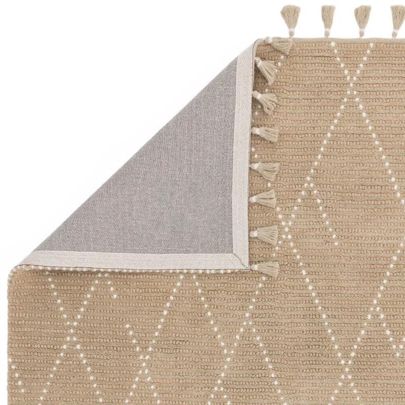 Beige woven rug with white diamond pattern and tassel edging, corner folded to show backing