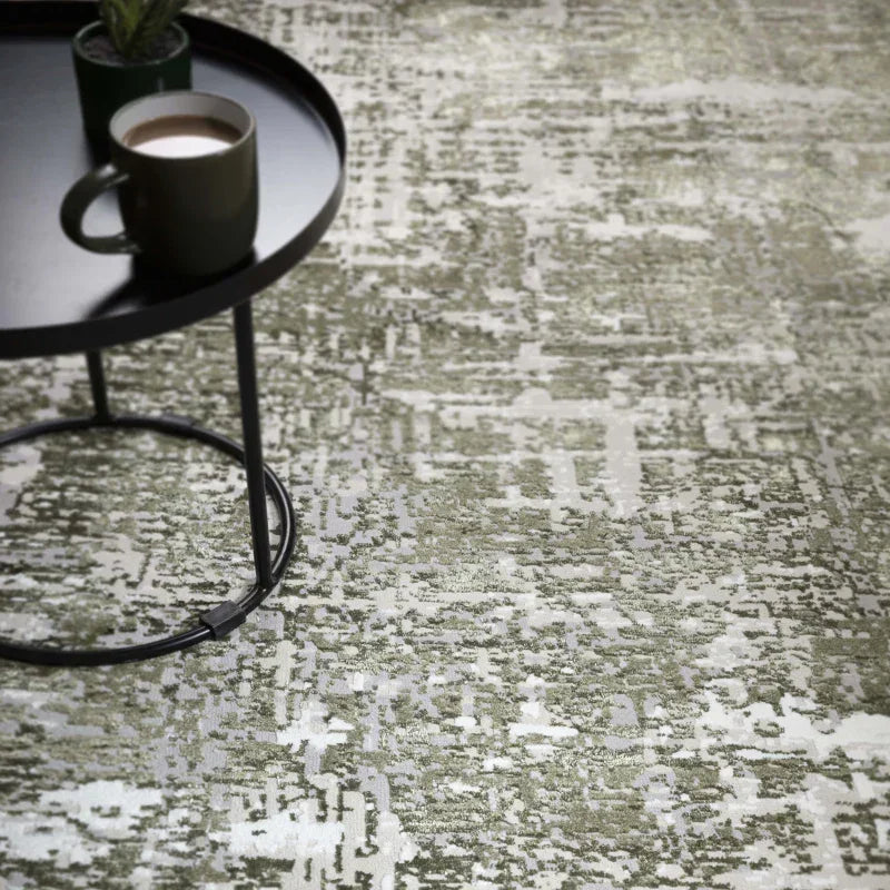 Modern abstract area rug with grey and green tones under round black metal coffee table