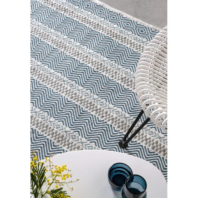 Grey and blue patterned rug under white chair and round coffee table with glassware