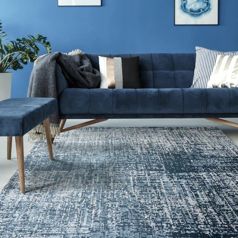 Velvet blue sofa with wooden legs, accent cushions and matching bench on patterned rug