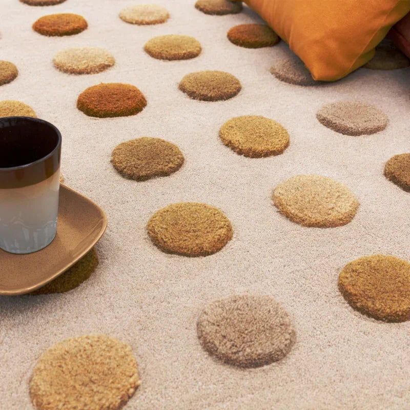 Beige polka dot rug with textured circles, cup and saucer, orange cushion on carpet