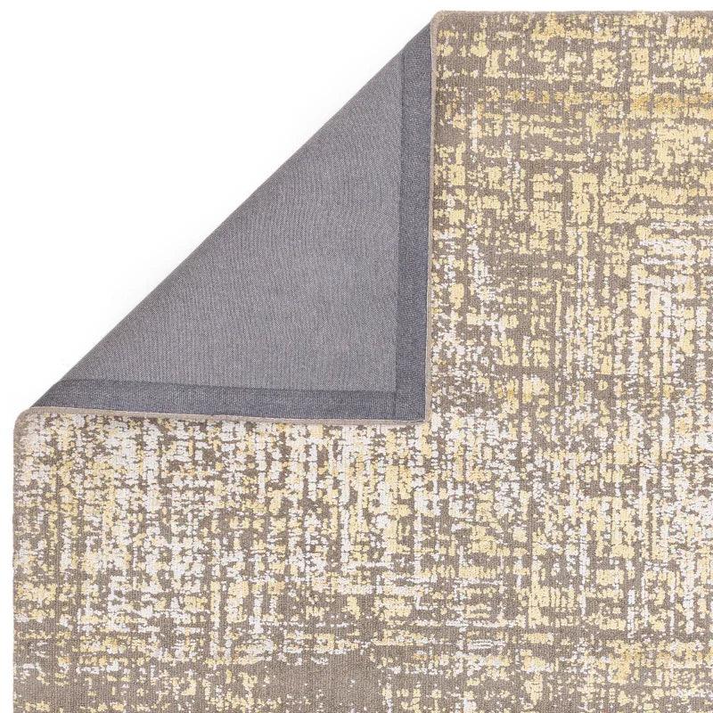 Abstract beige and yellow area rug with corner flipped to show grey backing