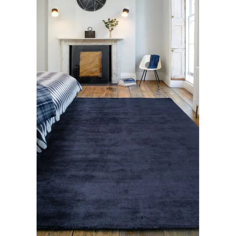 Large navy blue area rug on wooden bedroom floor beside bed