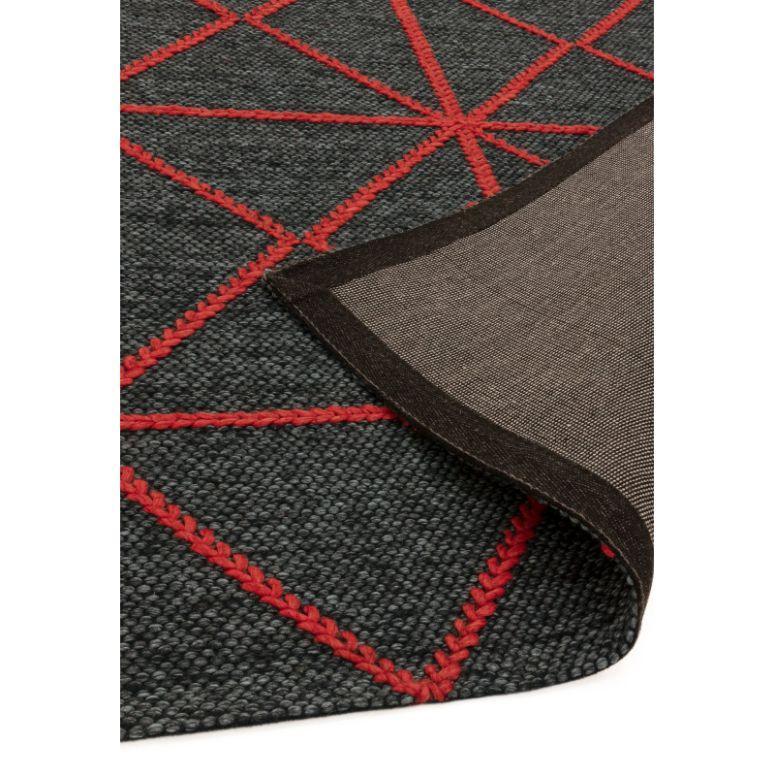 Dark grey woven rug with red geometric lines and corner folded to show backing