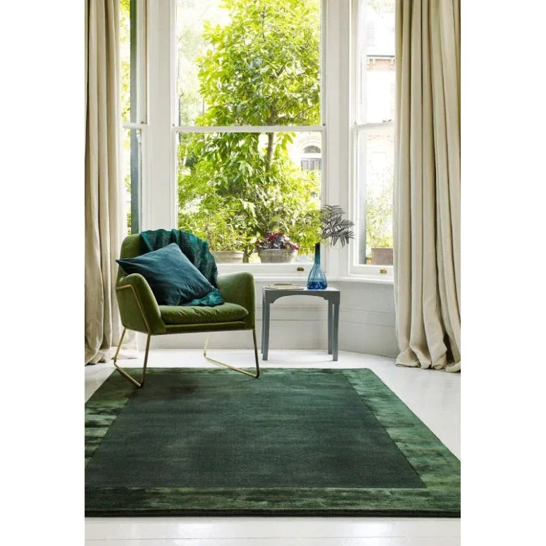 Green rug in living room with armchair, side table and large window with curtains