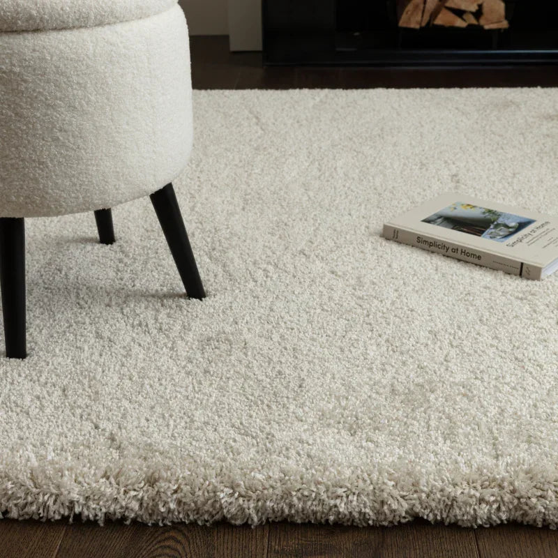 Cream shaggy rug on wooden floor with round stool and book