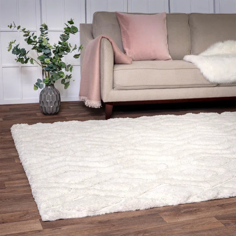 Cream shaggy rug on wood floor in living room with beige sofa and blush pink accents
