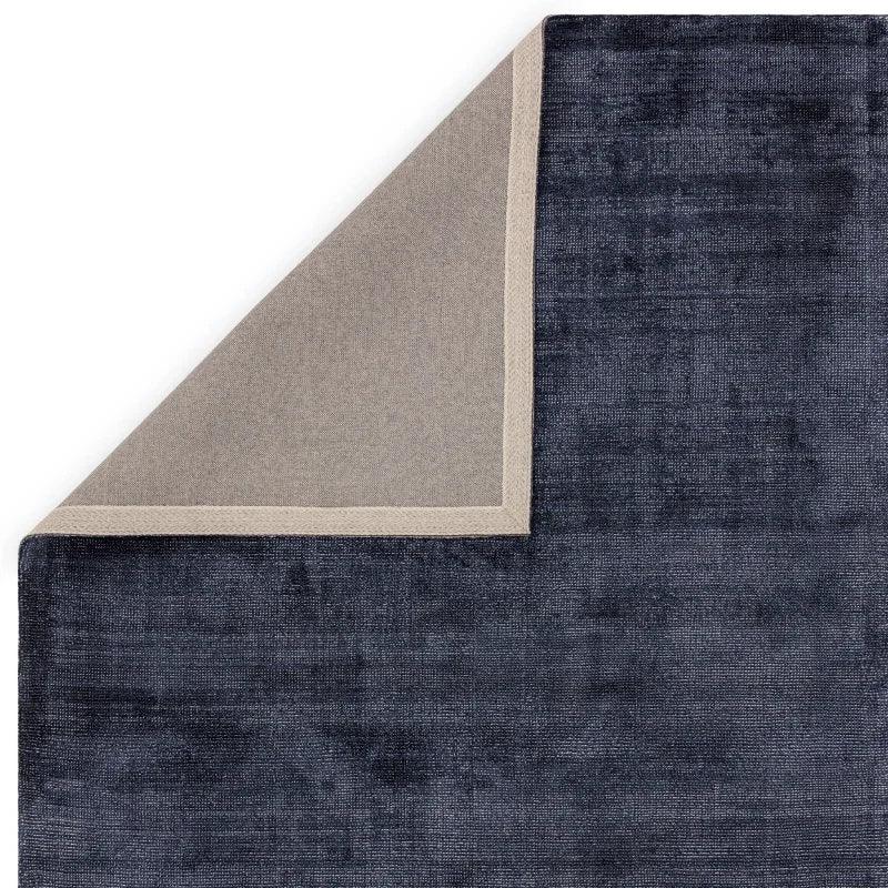 Navy blue area rug with corner flipped to reveal beige backing and stitched edge