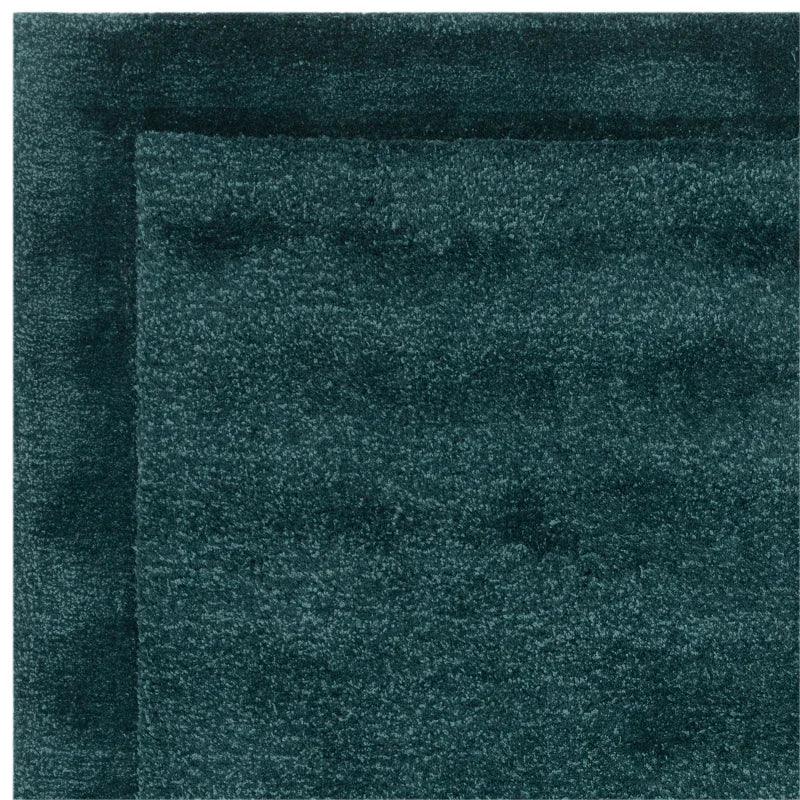Closeup of dark green plush rug with textured pile and subtle border design